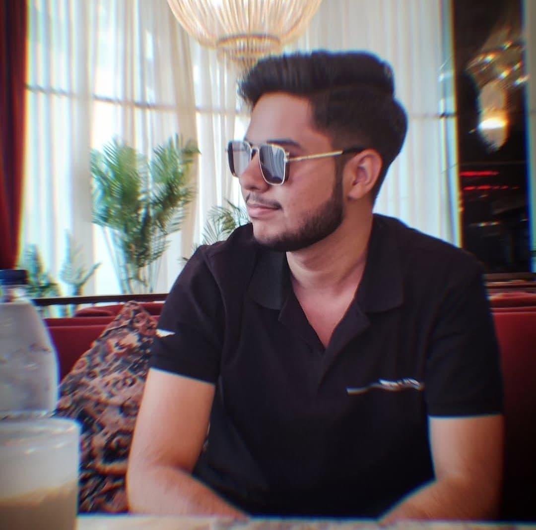Harshit sitting in a cafe wearing sunglasses, looking away from the camera